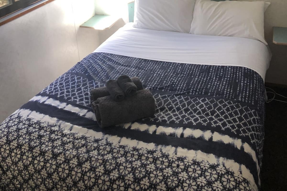 A bedroom with a bed, a window, a nightstand, and a wall-mounted light.