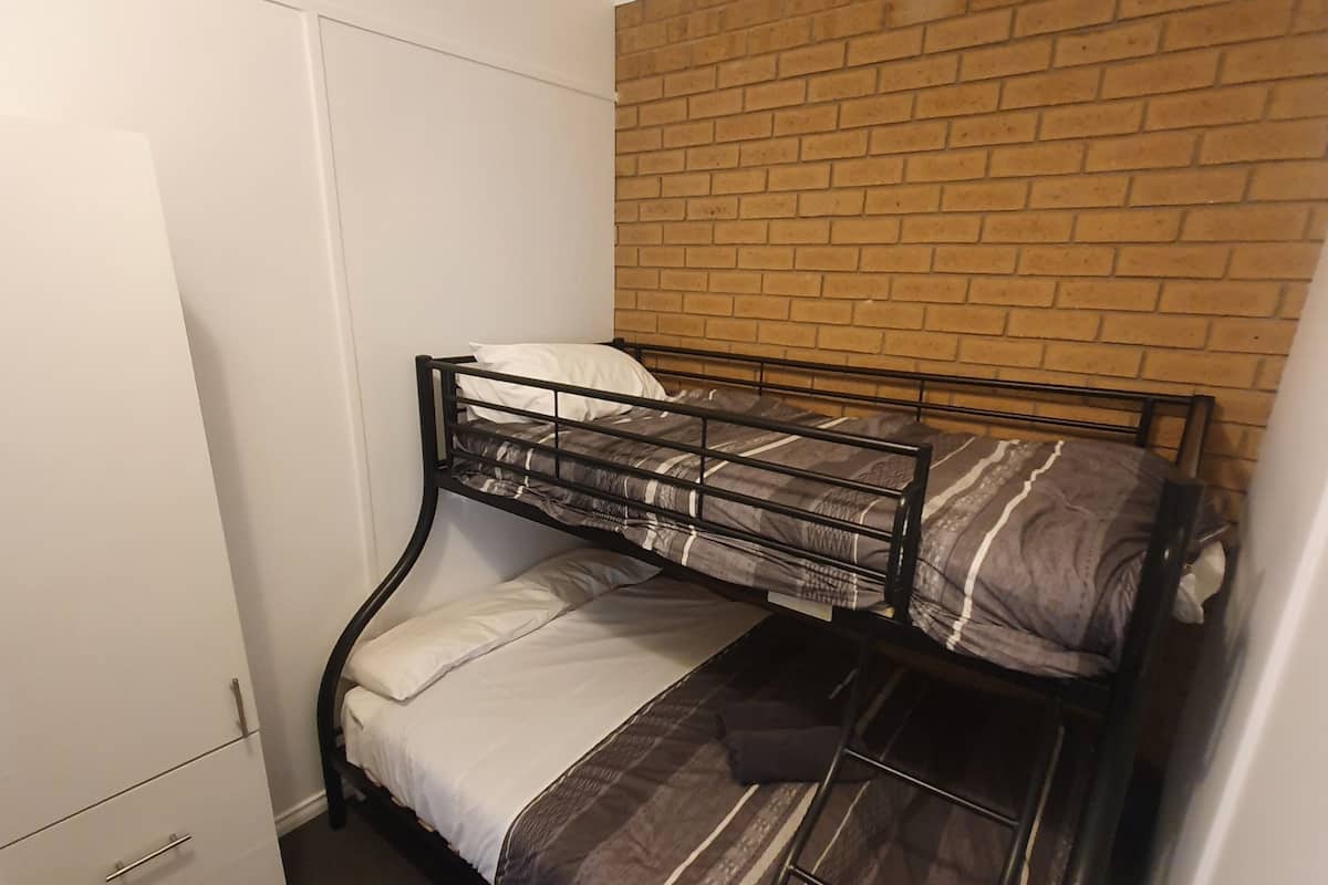 A bunk bed with a brick wall behind it, a white wardrobe, and a small heater on the floor.