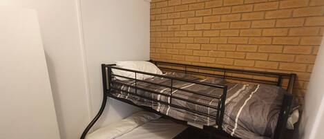 A bunk bed with a brick wall behind it, a white wardrobe, and a small heater on the floor.