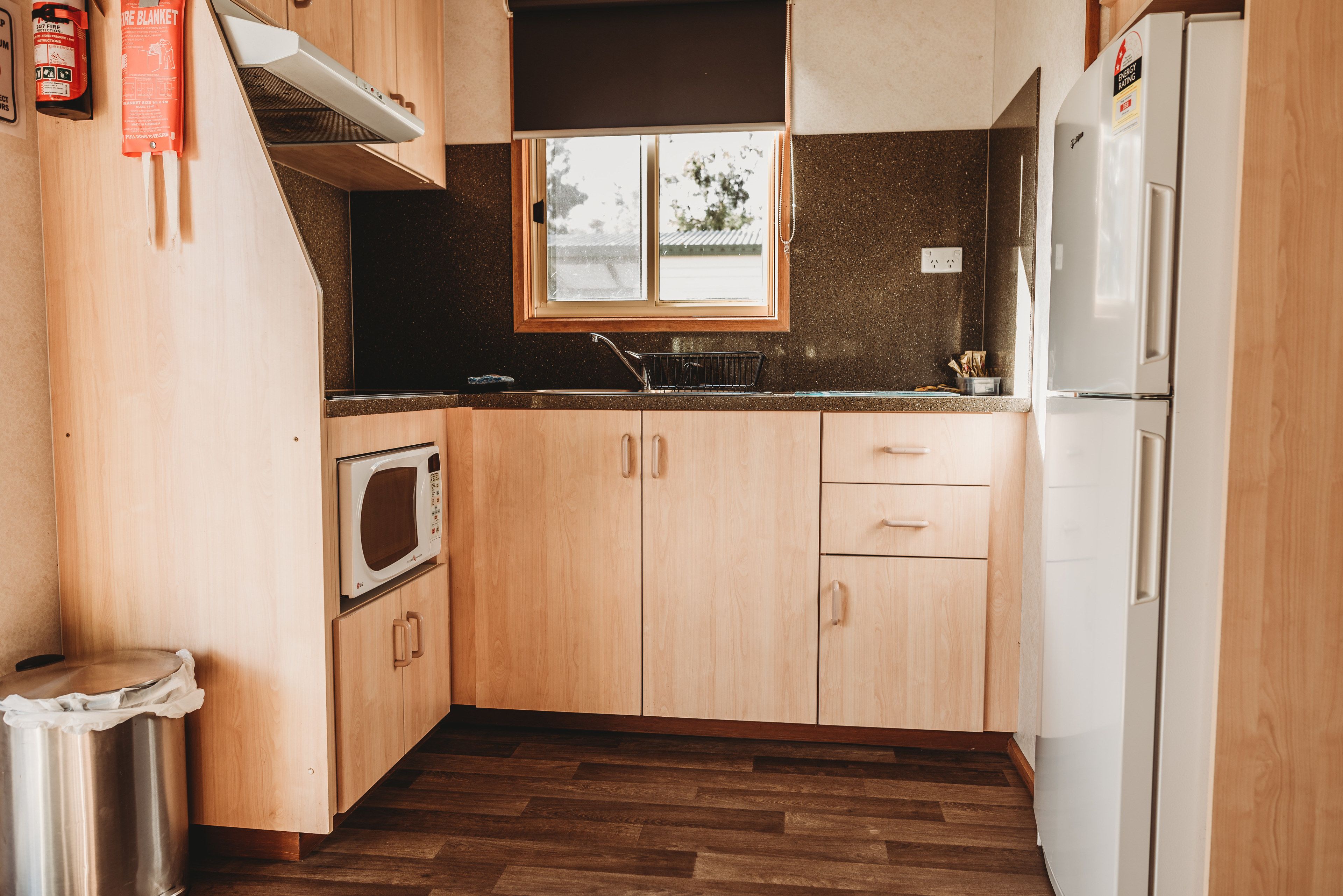 A compact kitchen with wooden cabinets, a microwave, a sink, and a refrigerator.