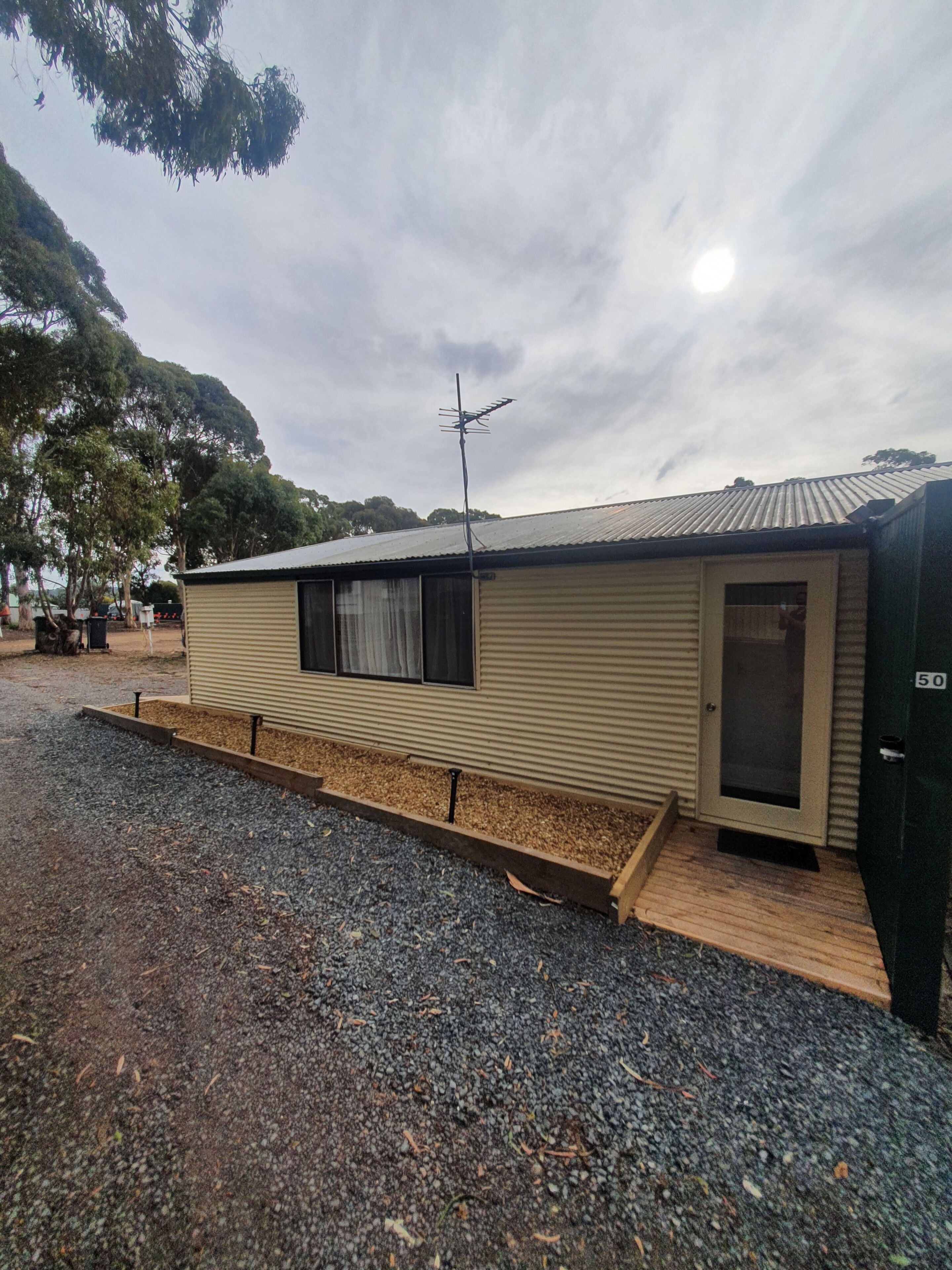 A single-story mobile home with a metal roof, a small porch, and a door with a number plate.