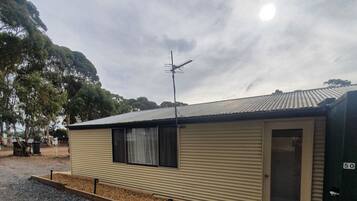 A single-story mobile home with a metal roof, a small porch, and a door with a number plate.