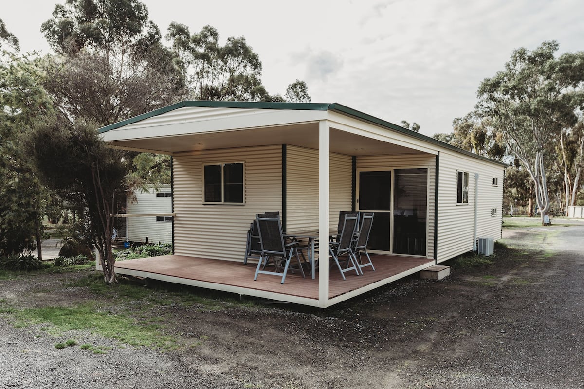 A single-story mobile home with a covered porch, two windows, and a door.