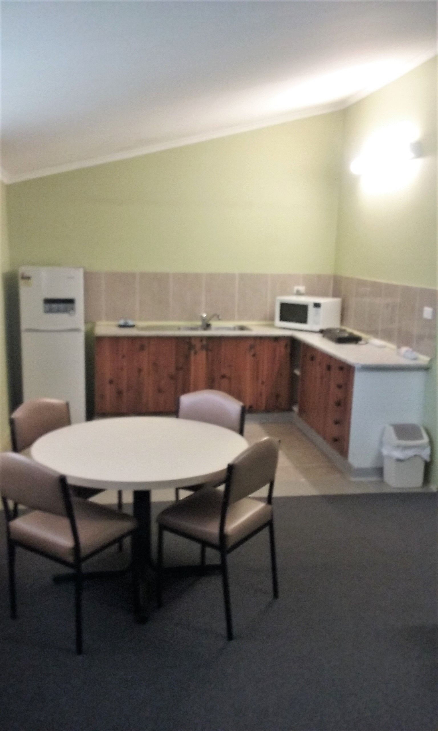 A compact kitchen with a dining table and chairs, a refrigerator, microwave, and cabinets.