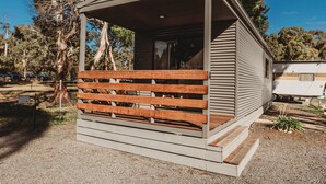 A small, single-story cabin with a wooden deck and a covered porch. - G'day Parks Ararat (Ararat)