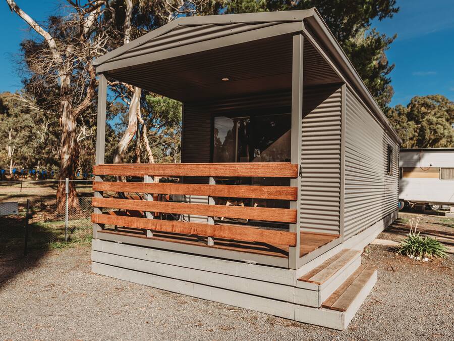 A small, single-story cabin with a wooden deck and a covered porch.
