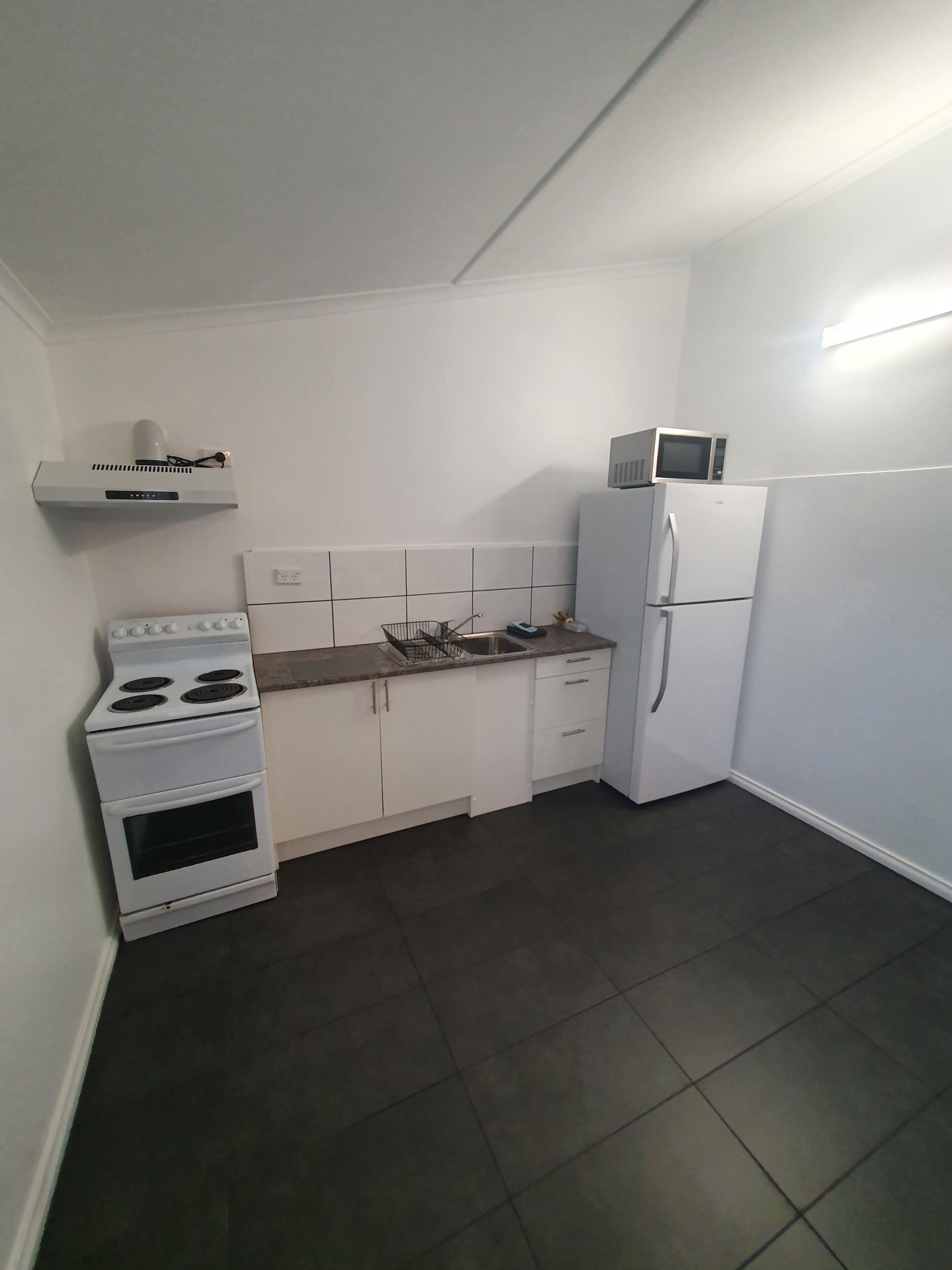 A compact kitchen with white cabinets, a stove, a microwave, and a refrigerator.