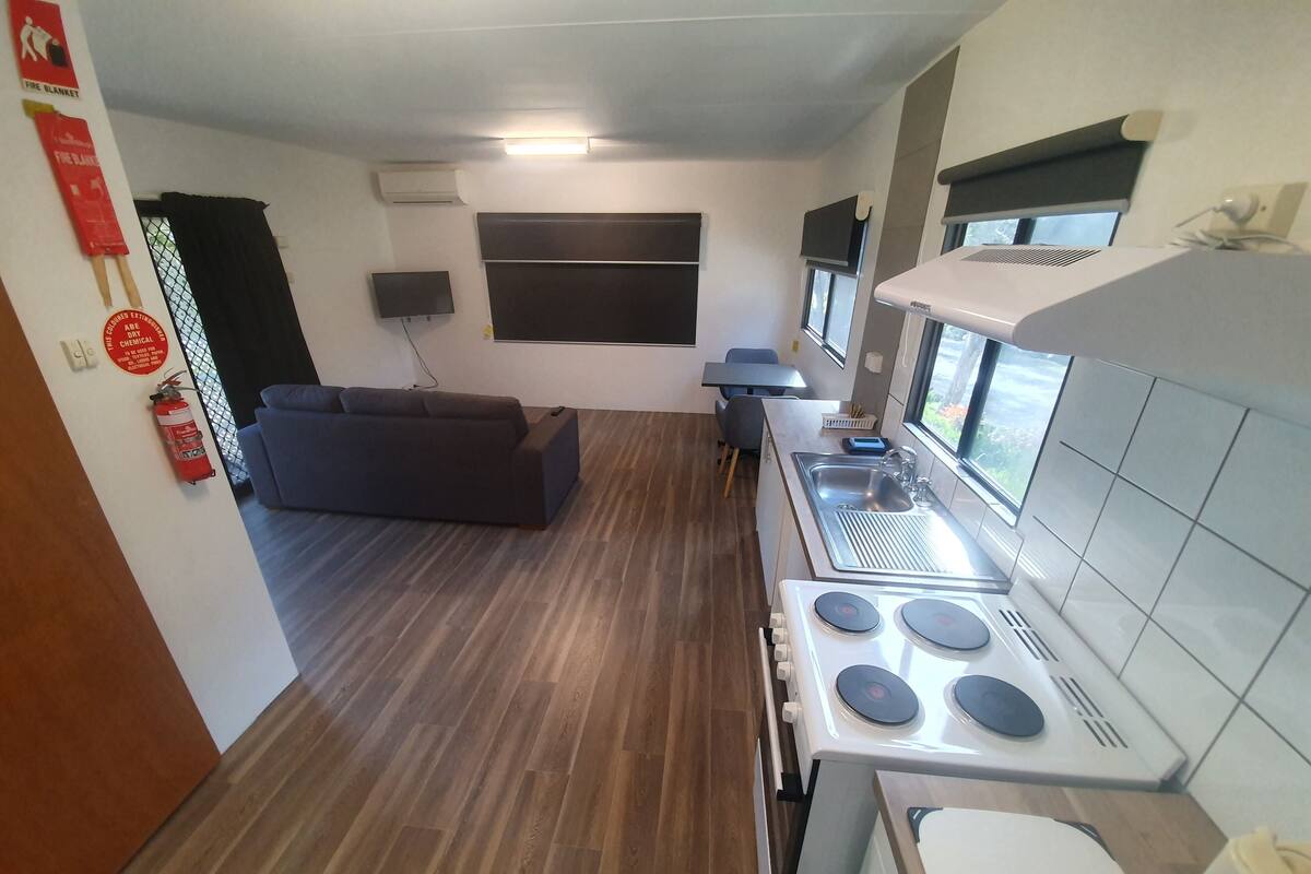A compact kitchen with a stove, sink, and a dining area with a sofa.