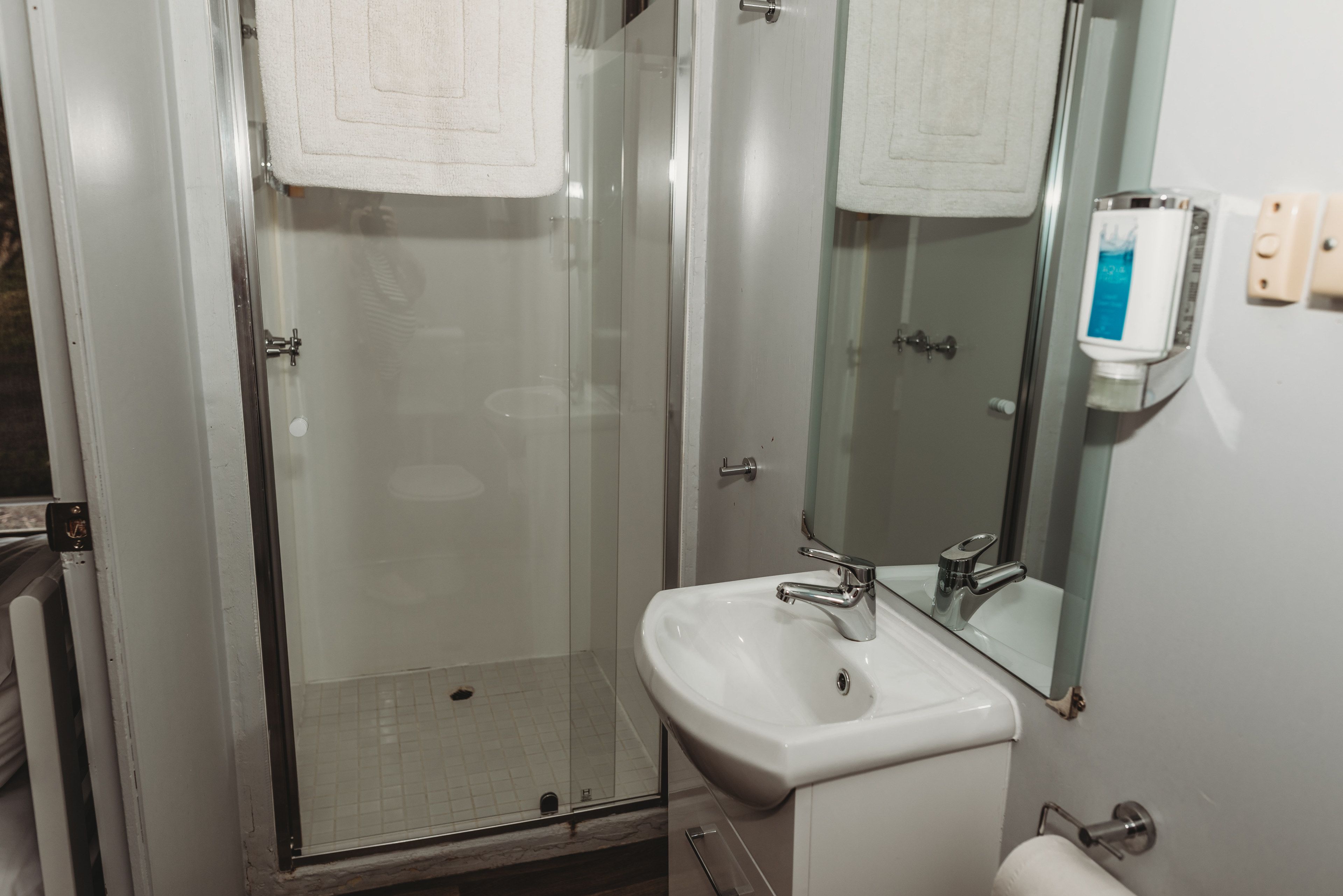 Un bagno con doccia vetrata, lavandino bianco e specchio.