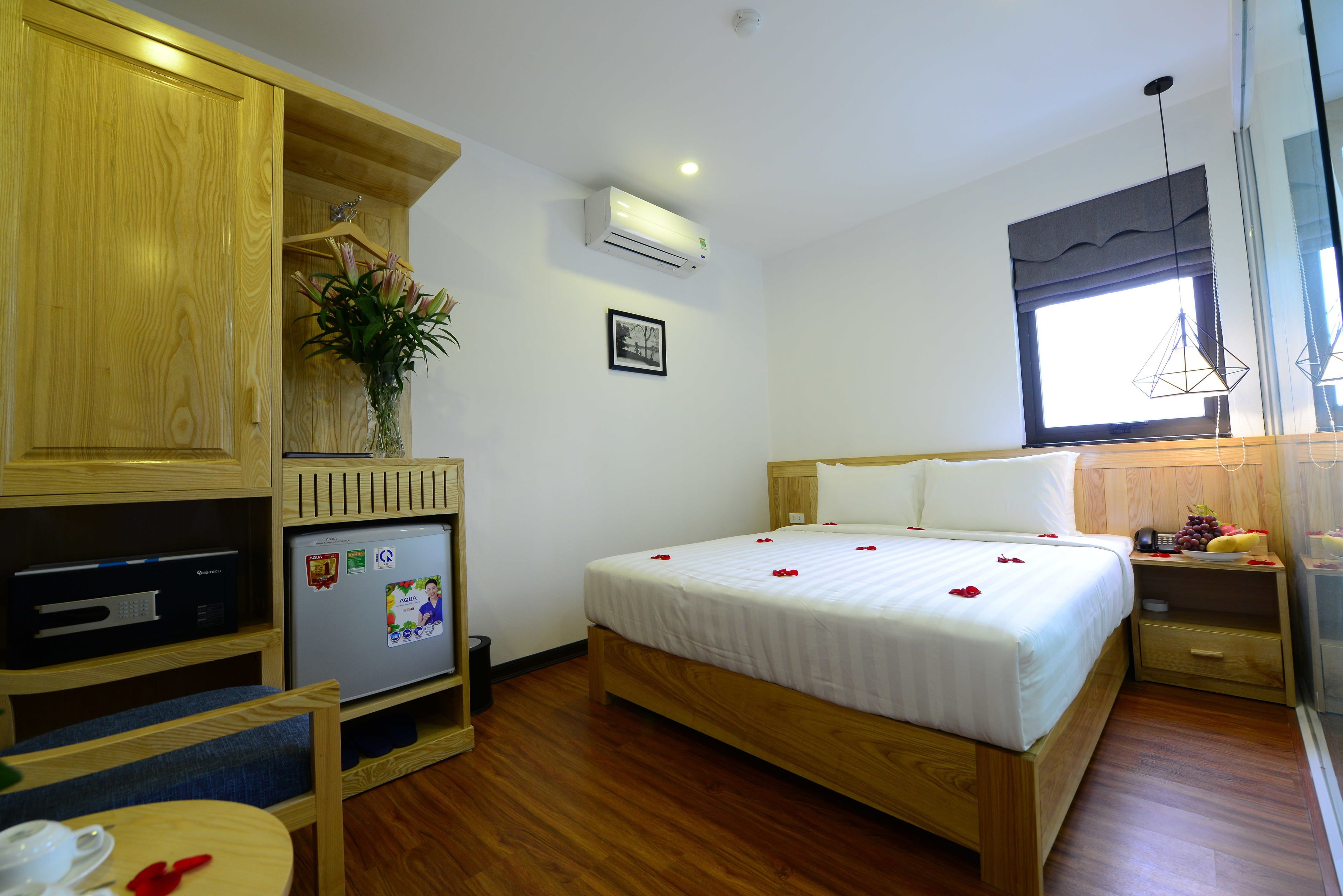 A hotel room with a wooden bed, a small desk with a computer, a refrigerator, and a window with a view.