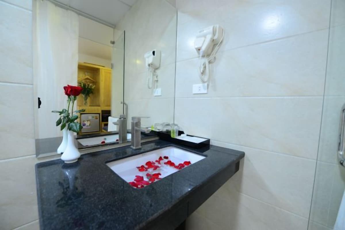 Un bagno con un lavabo in marmo, uno specchio, un vaso bianco con una rosa rossa e un asciugamano appeso al muro.