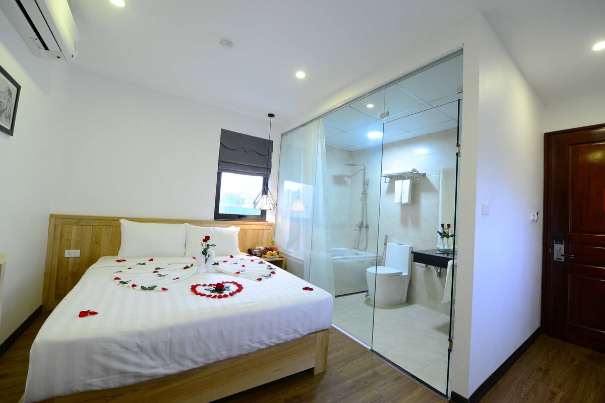 Ein Hotelzimmer mit Bett, einer in Glas eingefassten Duschkabine, einem Holz-Kopfteil und einem Fenster.