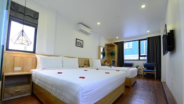 A hotel room with a large bed, bedside tables, a small desk, a chair, a TV, and a window with curtains.