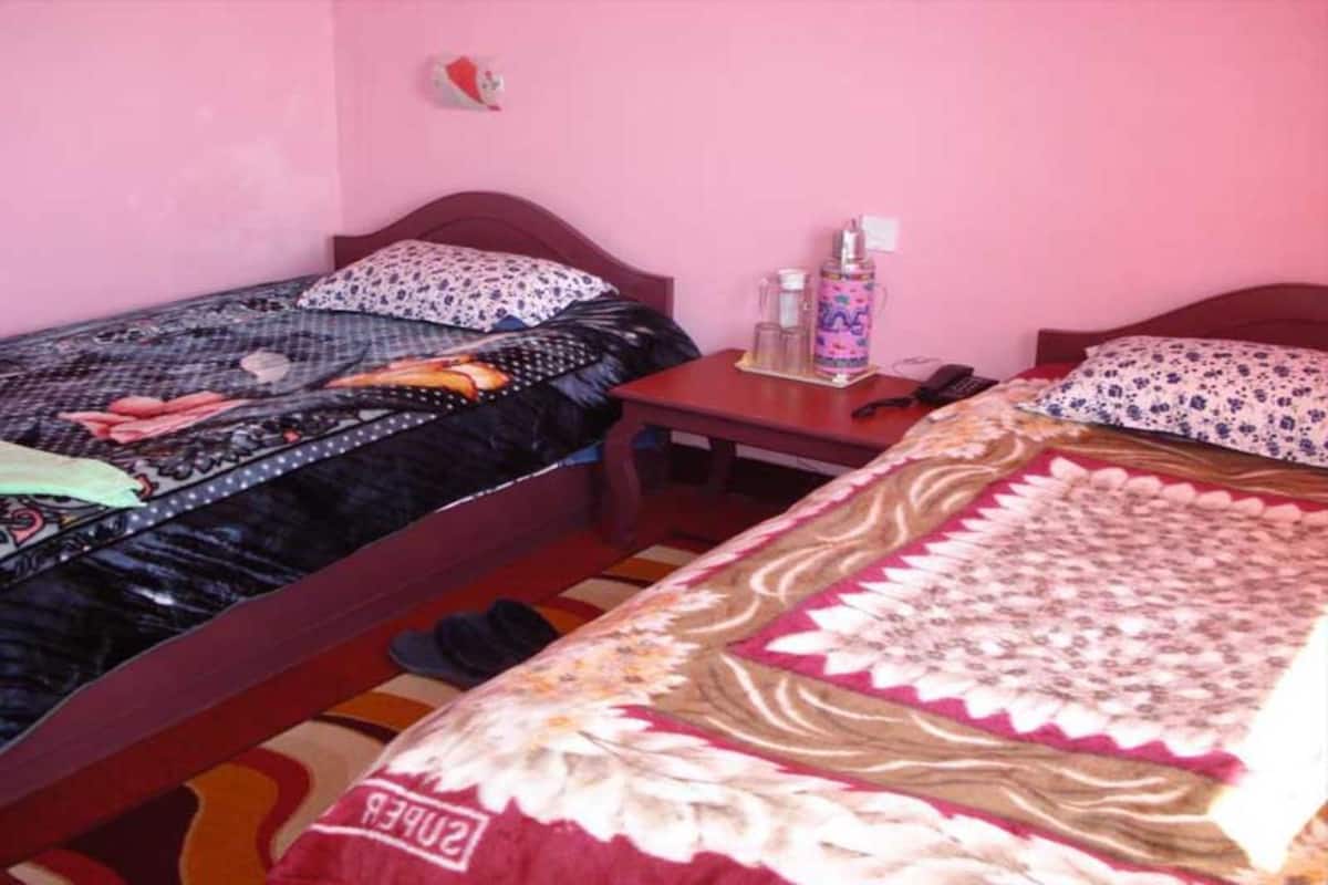 Quarto com duas camas, uma mesinha e um adorno na parede.