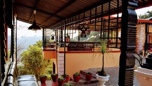 A covered outdoor seating area with potted plants, a bench, and a view of the mountains.