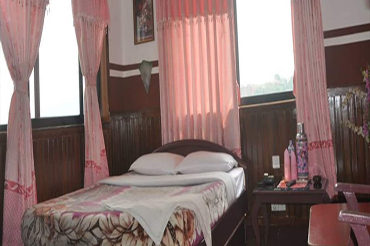 Quarto com cama, cortinas, mesa de cabeceira e escrivaninha com cadeira.