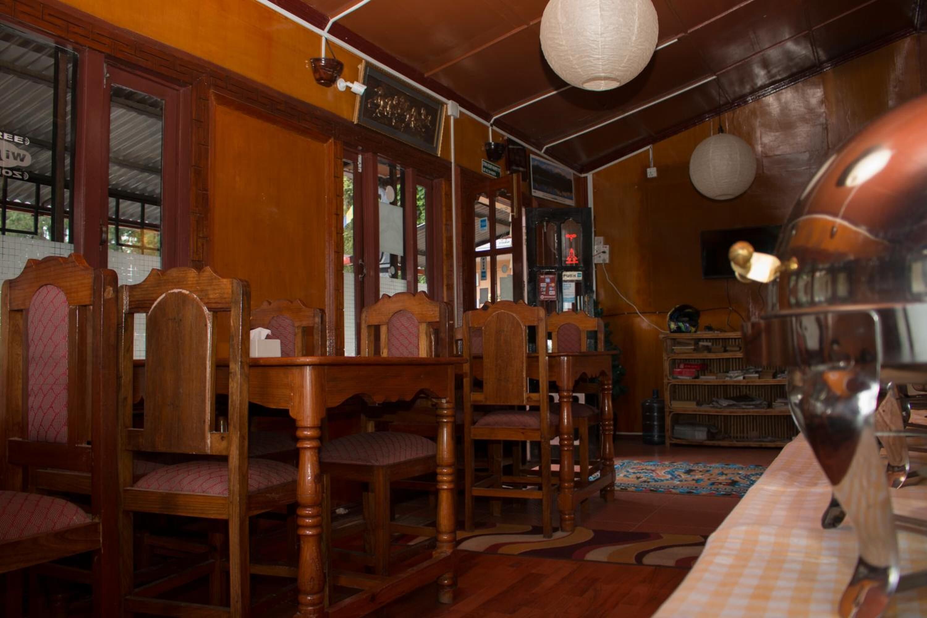 Un interior de madera con varias sillas y una mesa de madera, una estantería y una alfombra estampada.