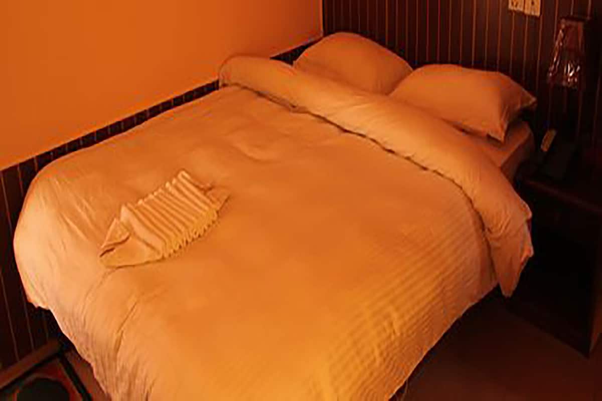 A bed with a white comforter and pillows, a bedside table with a lamp, and a striped wall.