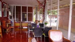 A dining area with a red-tiled floor, a glass table, and wicker chairs. - Somjainuk Resort 2 (Pluak Daeng)