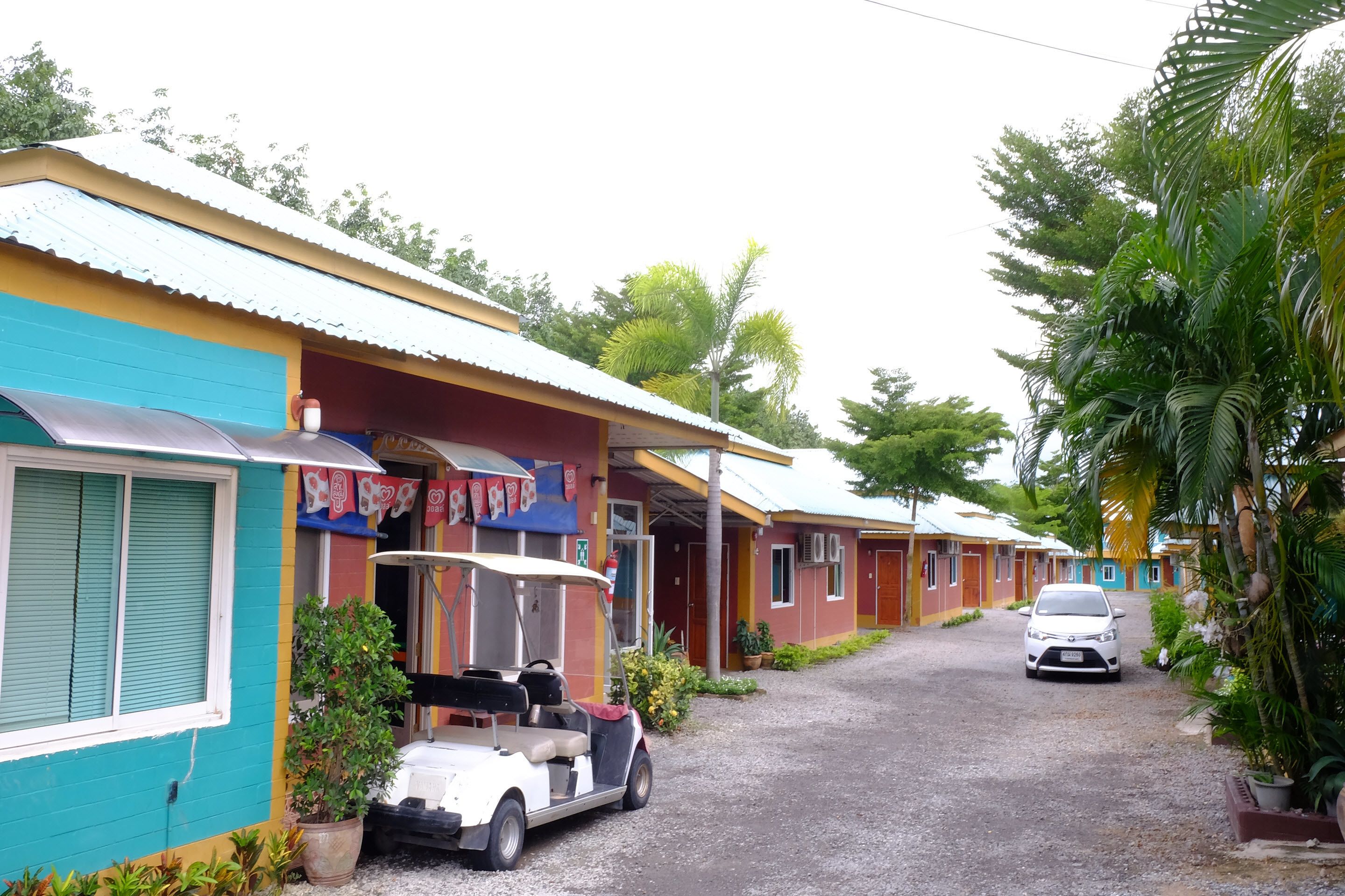 A row of colorful buildings with a gravel driveway, a golf cart, and a car parked in front.