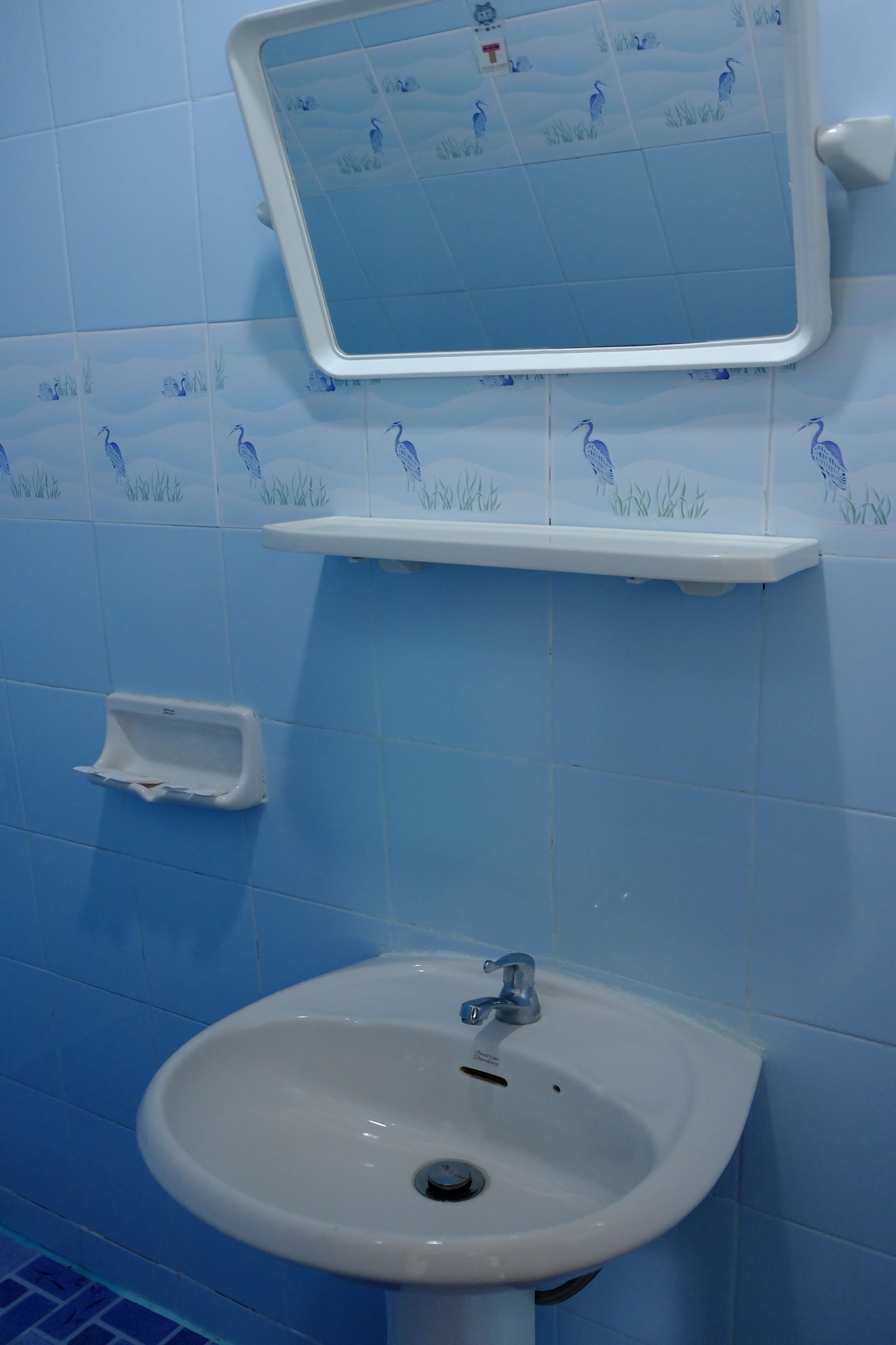 A bathroom with blue tiles, a white sink, and a mirror above it.