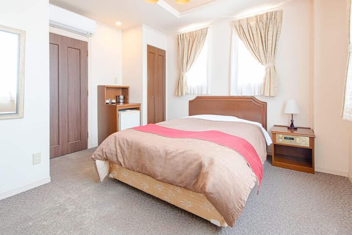 Una habitación de hotel con una cama, una mesita de noche, un armario y una ventana con cortinas.