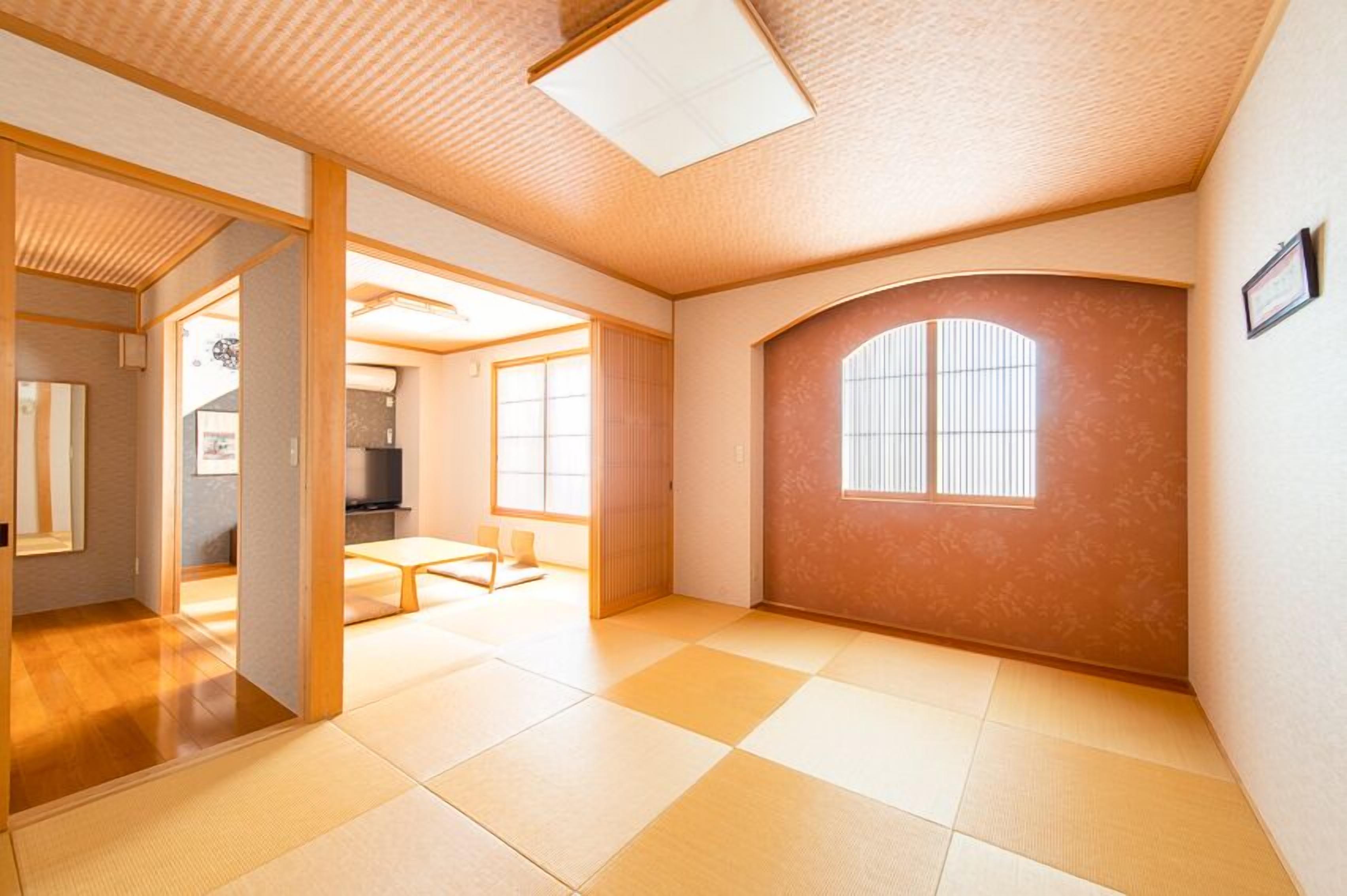 A room with tatami flooring, a sliding door, a low ceiling with a skylight, and a large window with a view.