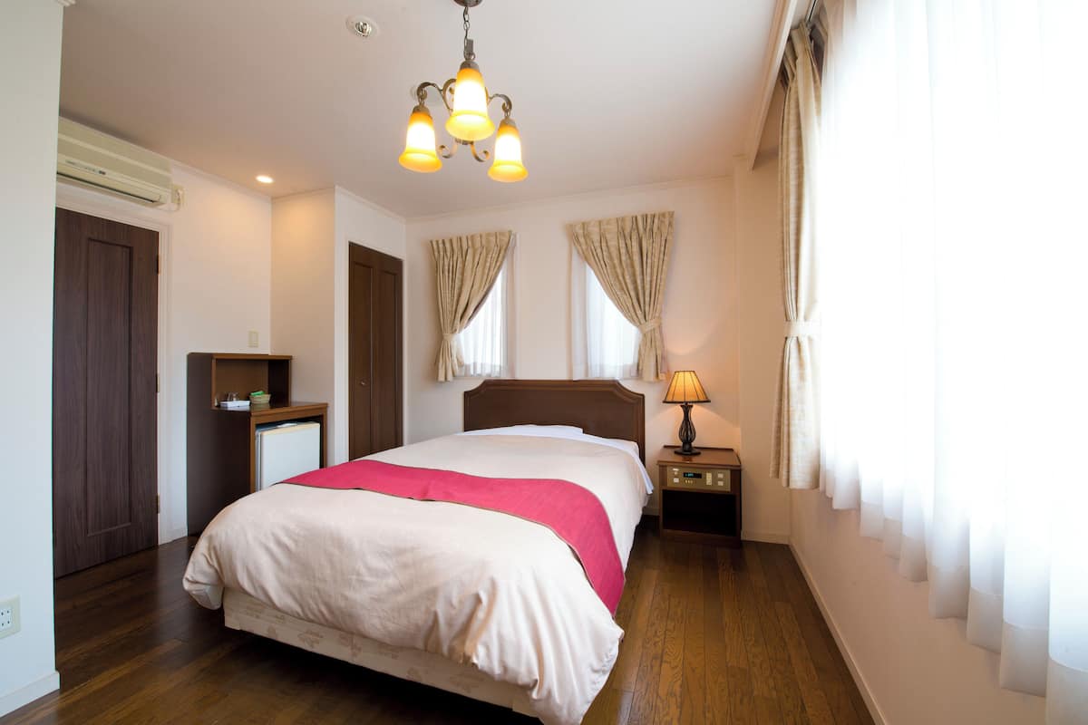 Una habitación de hotel con cama, mesita de noche, lámpara y cortinas.