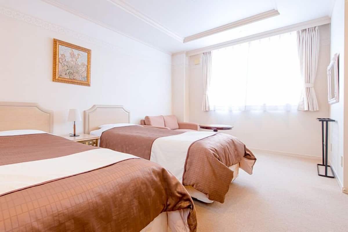Habitación de hotel con dos camas, una mesita de noche con lámpara, un cuadro en la pared y una ventana con cortinas.