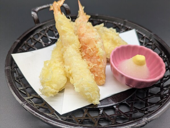 Una bandeja con tres porciones de tempura, un pequeño tazón rosa con una cucharada de salsa y una servilleta blanca.