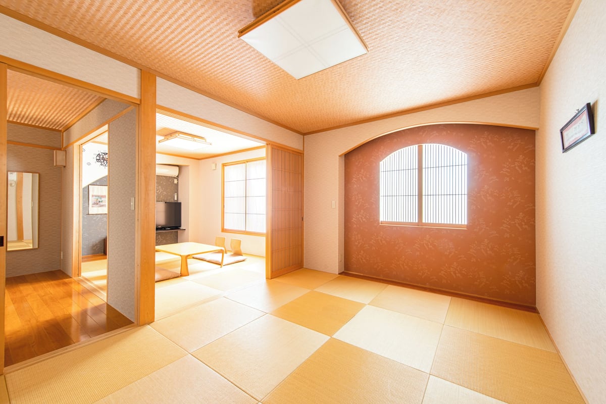 Una habitación con suelo de tatami, una puerta corredera, una pequeña mesa y una ventana con barrotes.