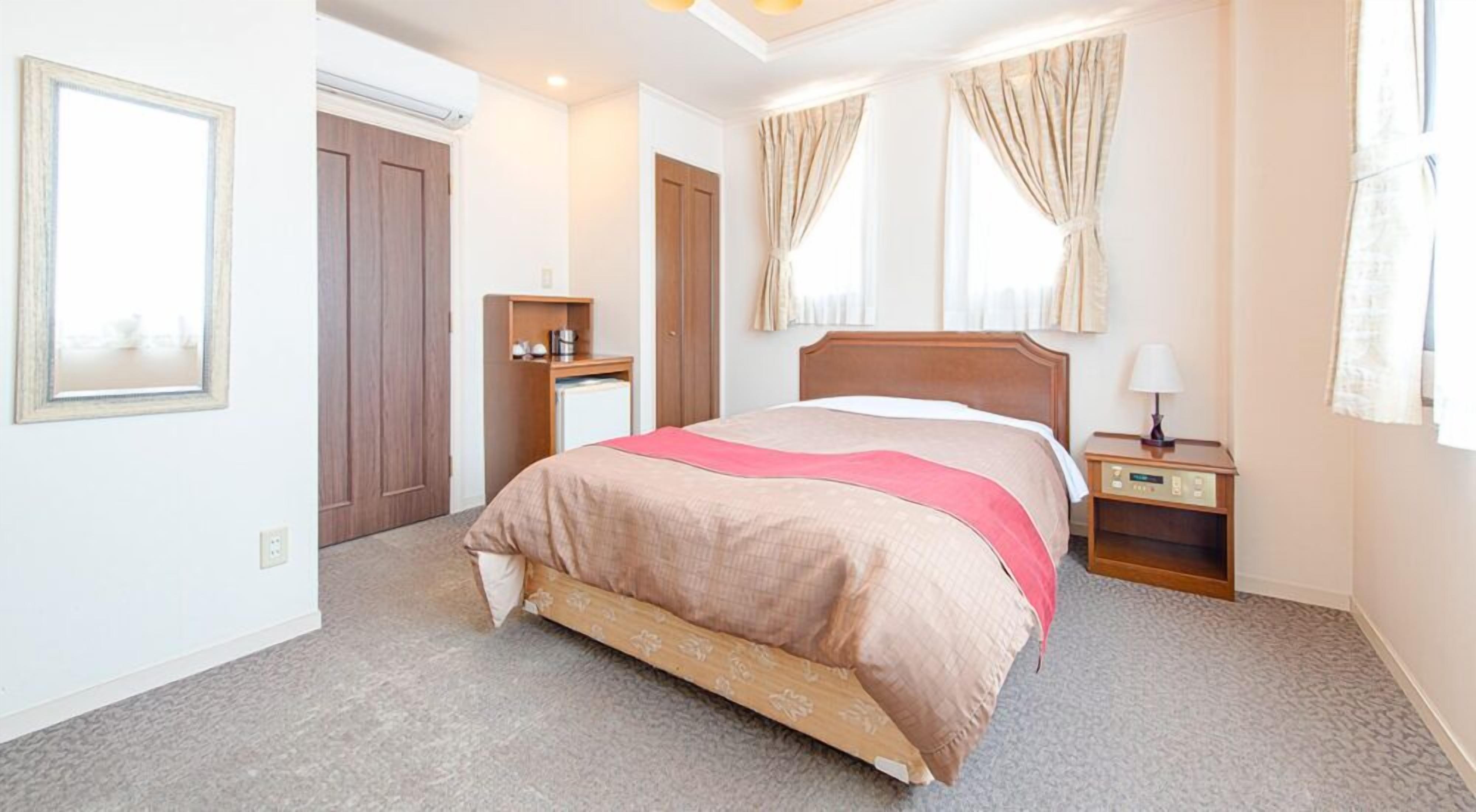 A hotel room with a bed, bedside tables, a wardrobe, and a window with curtains.