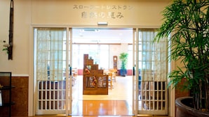 Un intérieur japonais traditionnel avec des portes coulissantes, un comptoir d’accueil en bois et une grande plante en pot.
