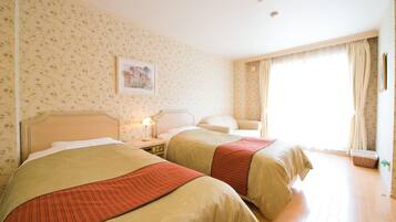 Habitación de hotel con dos camas, papel tapiz floral, un cuadro en la pared y una ventana con cortinas.