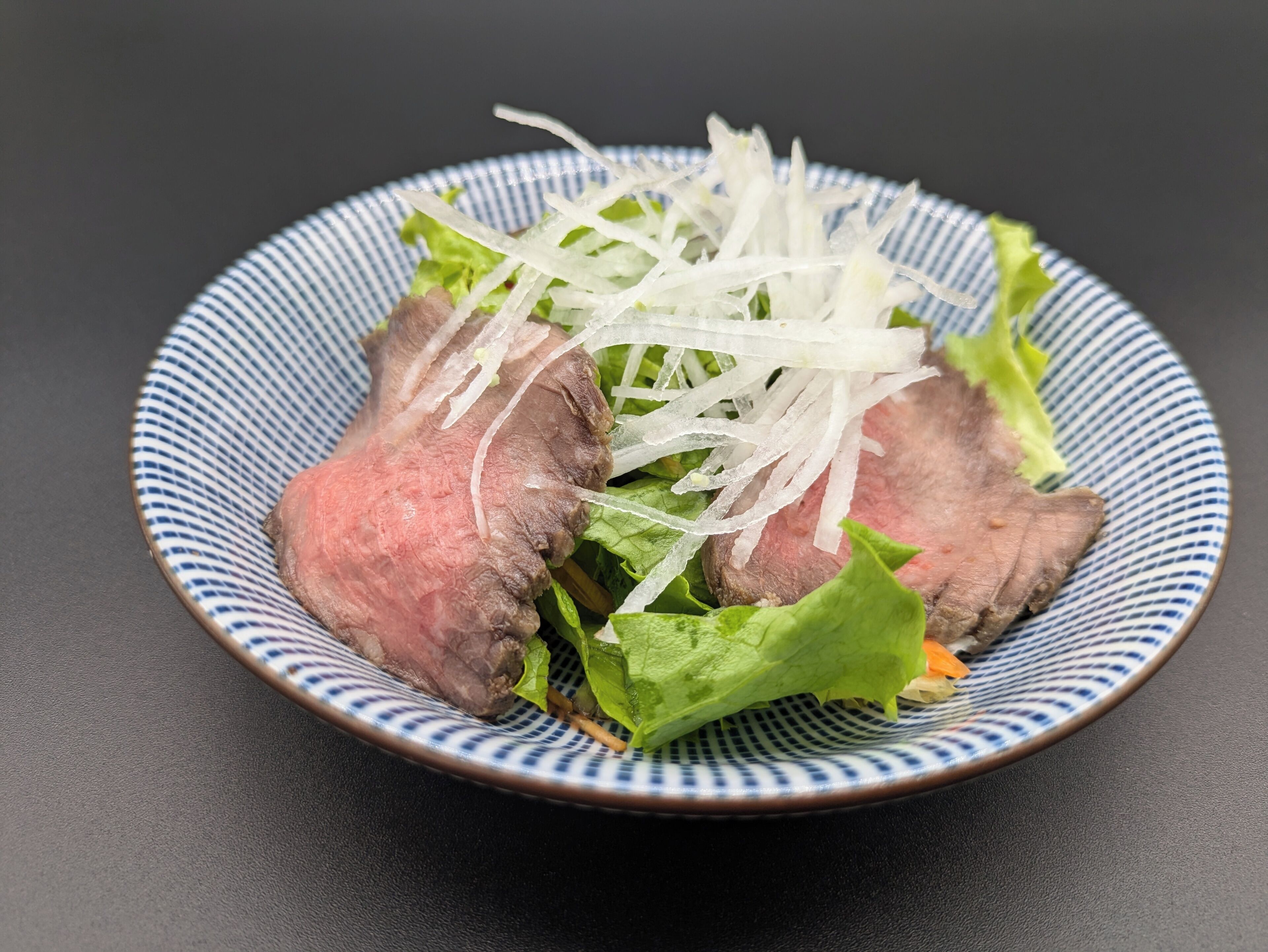 A plate with sliced meat and shredded vegetables on a blue and white patterned plate.