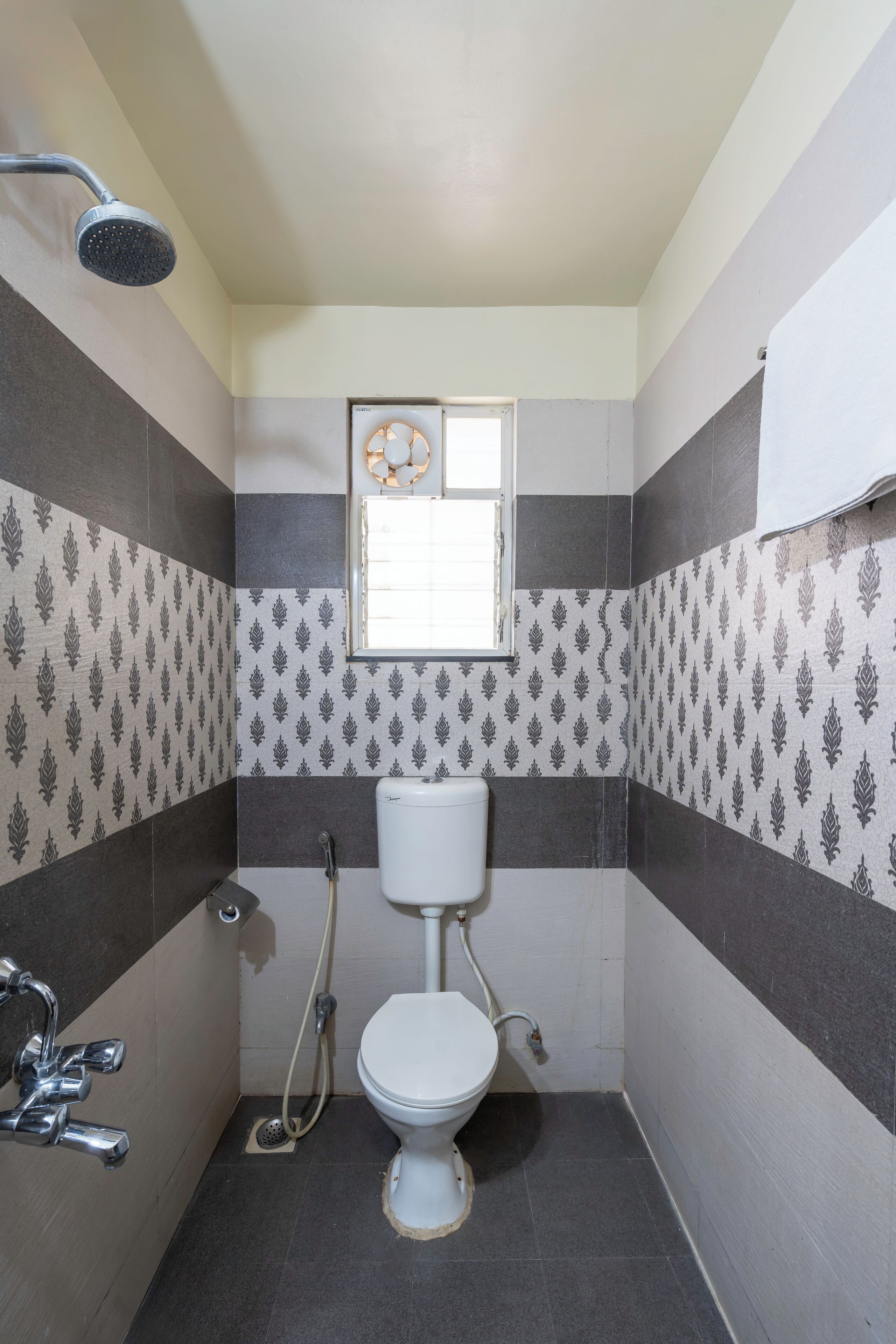 A bathroom with a toilet, shower, and a window.