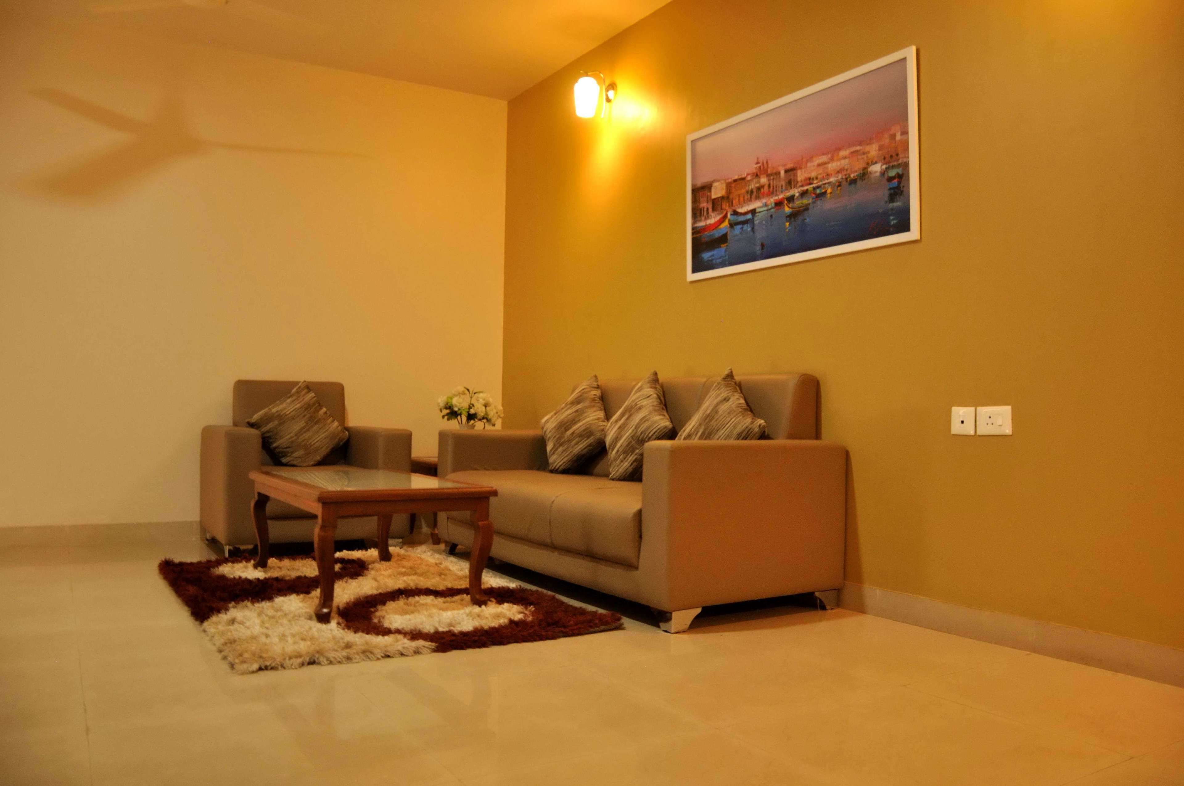 A living room with a sofa, a coffee table, and a rug. There is a painting on the wall and a ceiling fan.