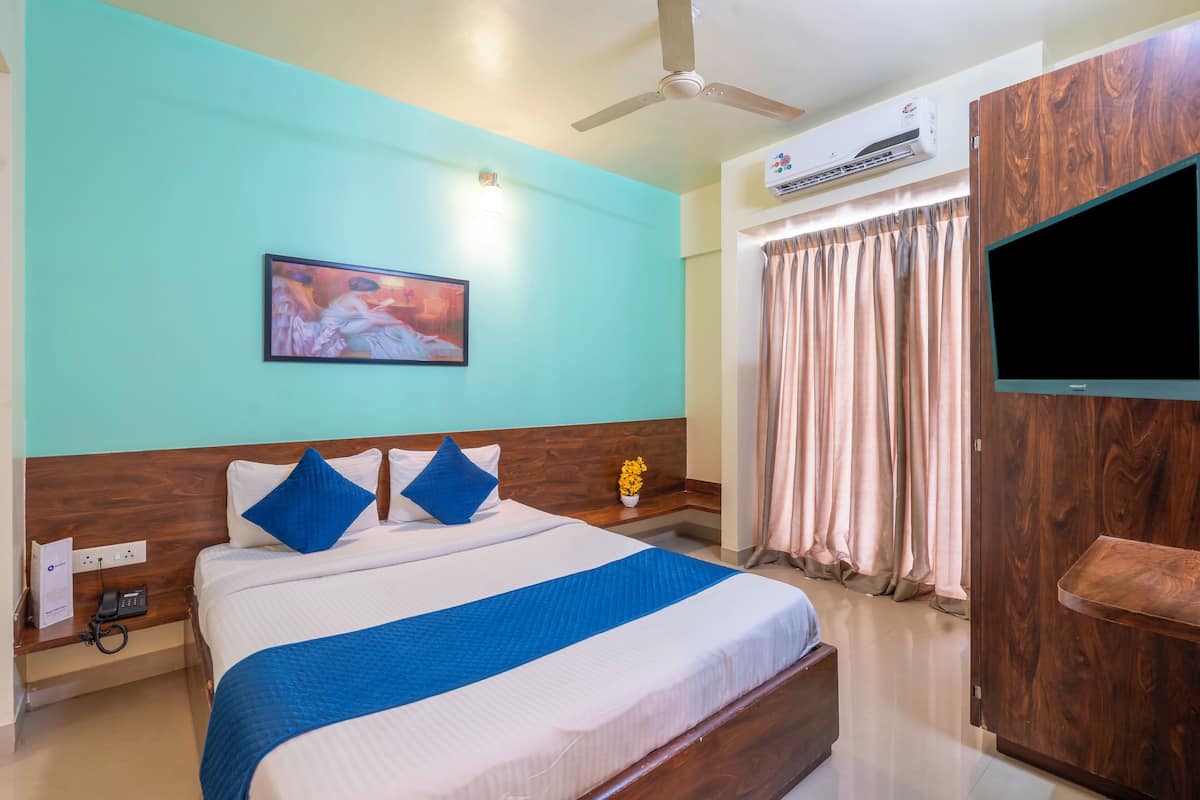 Habitación de hotel con cama, televisor de pantalla plana, equipo de aire acondicionado, ventilador de techo y ventana con cortinas.