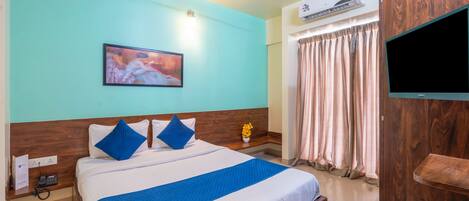 A hotel room with a bed, a flat-screen TV, an air conditioning unit, a ceiling fan, and a window with curtains.