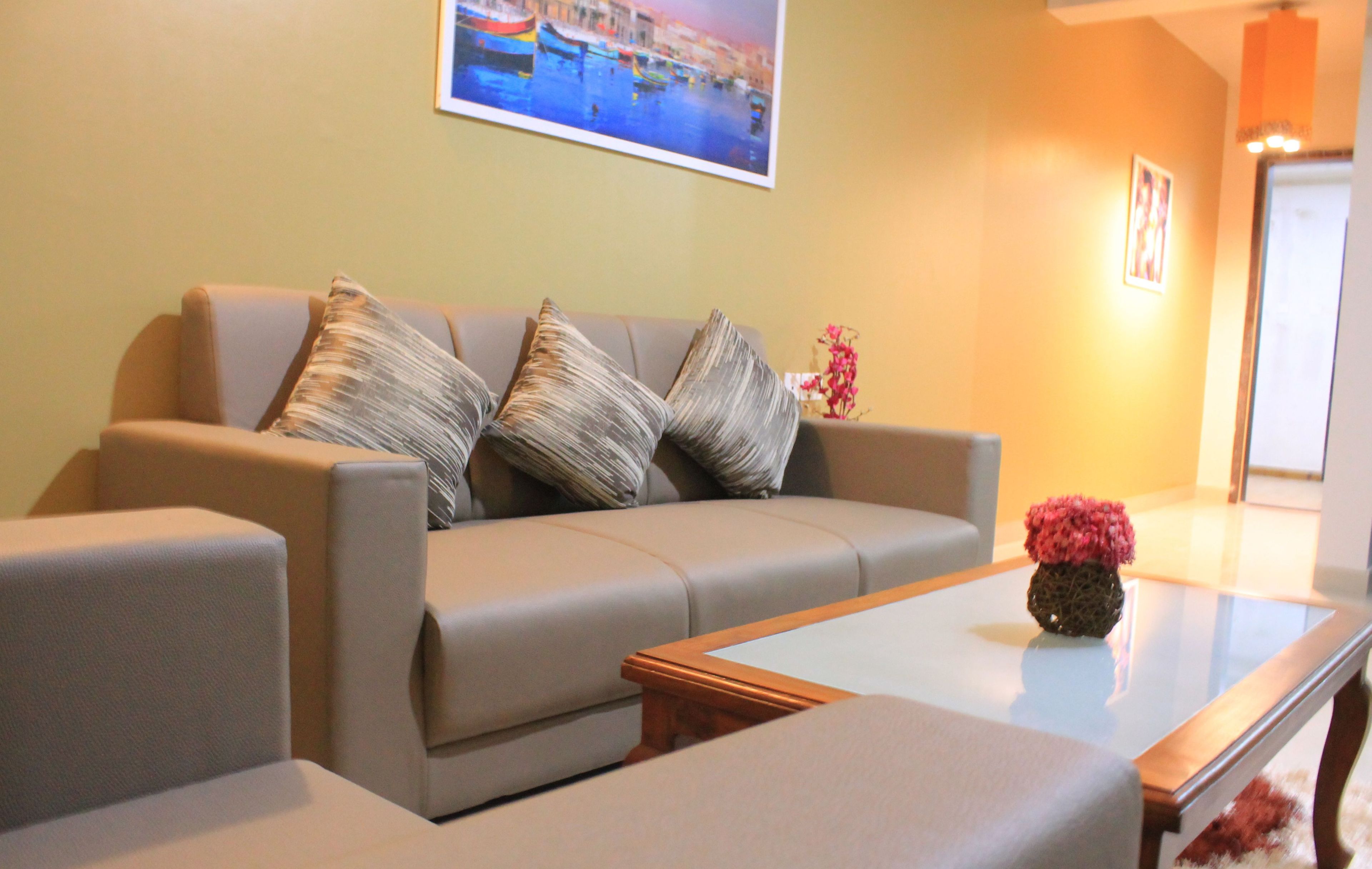 A modern living room with a beige sofa, two matching armchairs, a glass coffee table, and a framed cityscape picture on the wall.