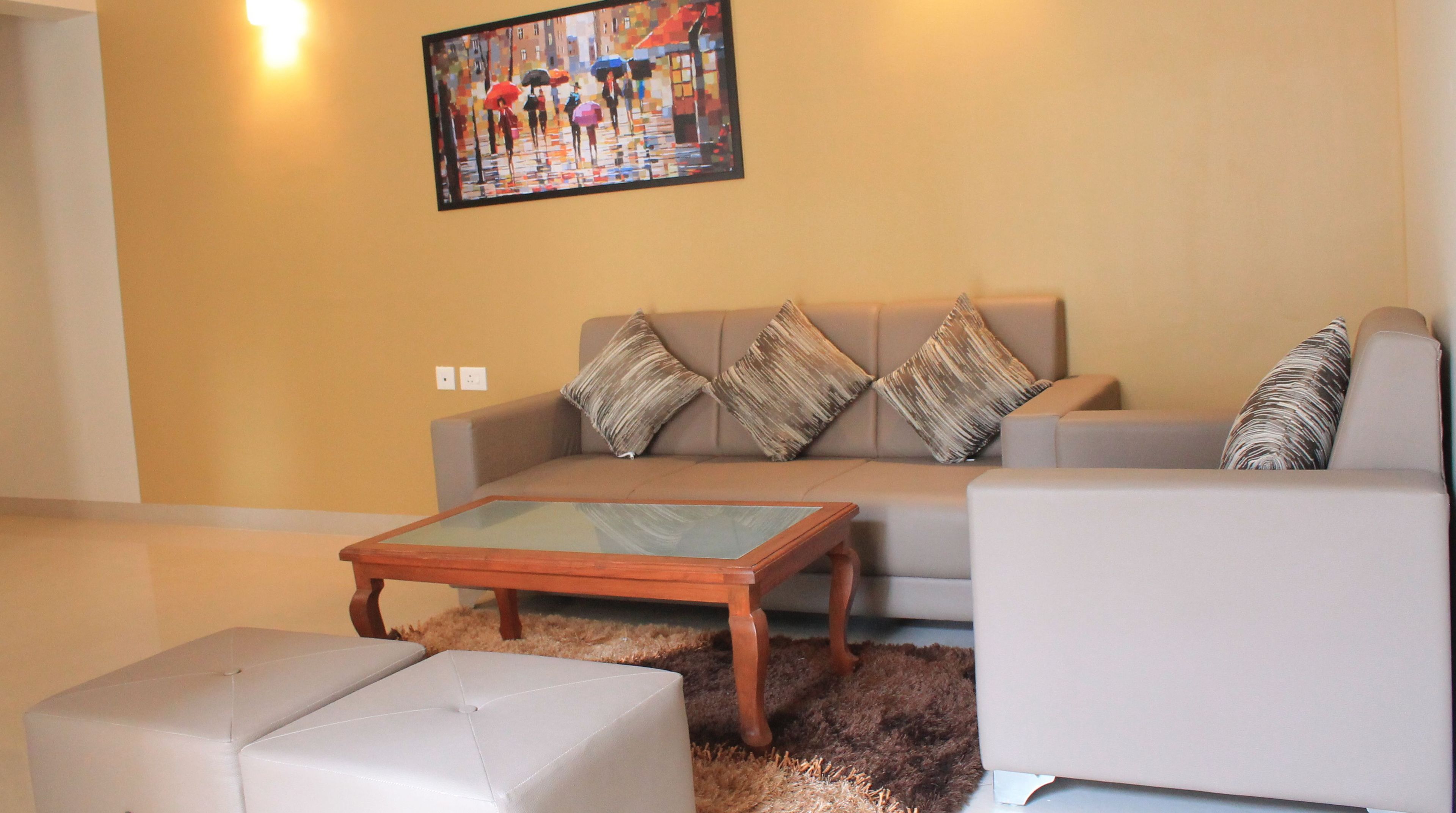A living room with a beige sofa, a glass coffee table, and two white ottomans.