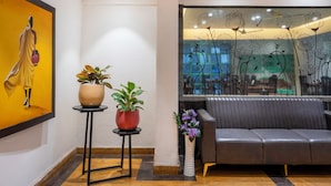 Un interior moderno con un sofá, dos plantas en macetas y un panel de vidrio decorativo con motivos florales.