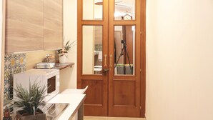 A narrow hallway with a ceiling fan, a wooden door with glass panels, and a kitchen area with a microwave and potted plants. - B&B Pietrarsa (Portici)