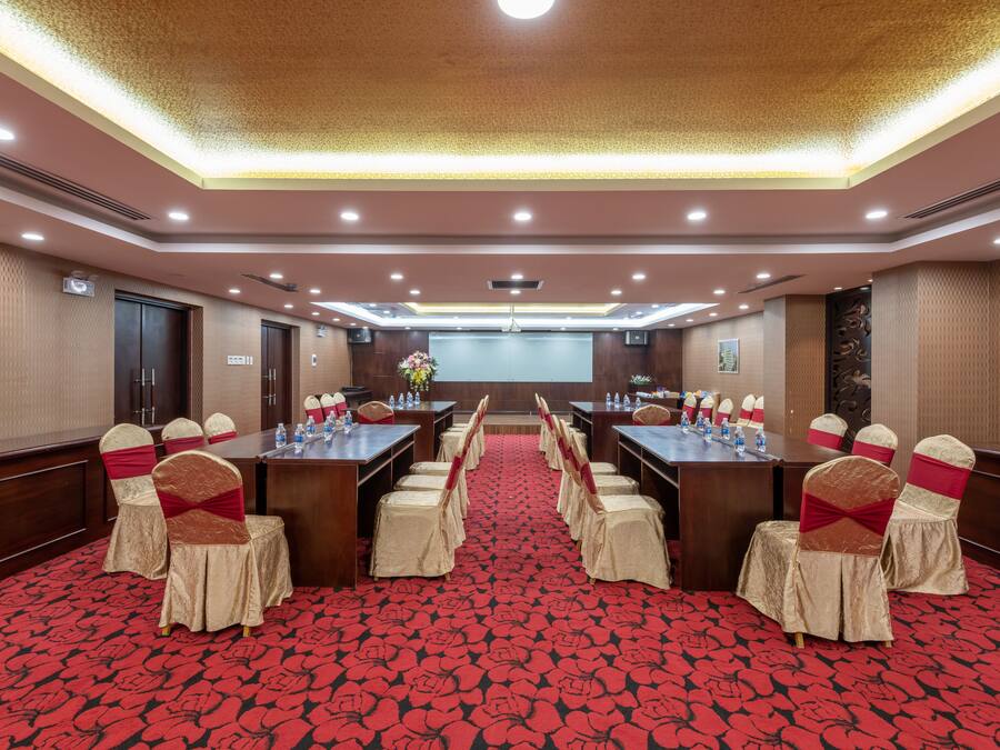 A conference room with a long table, chairs with red sashes, and a red patterned carpet.
