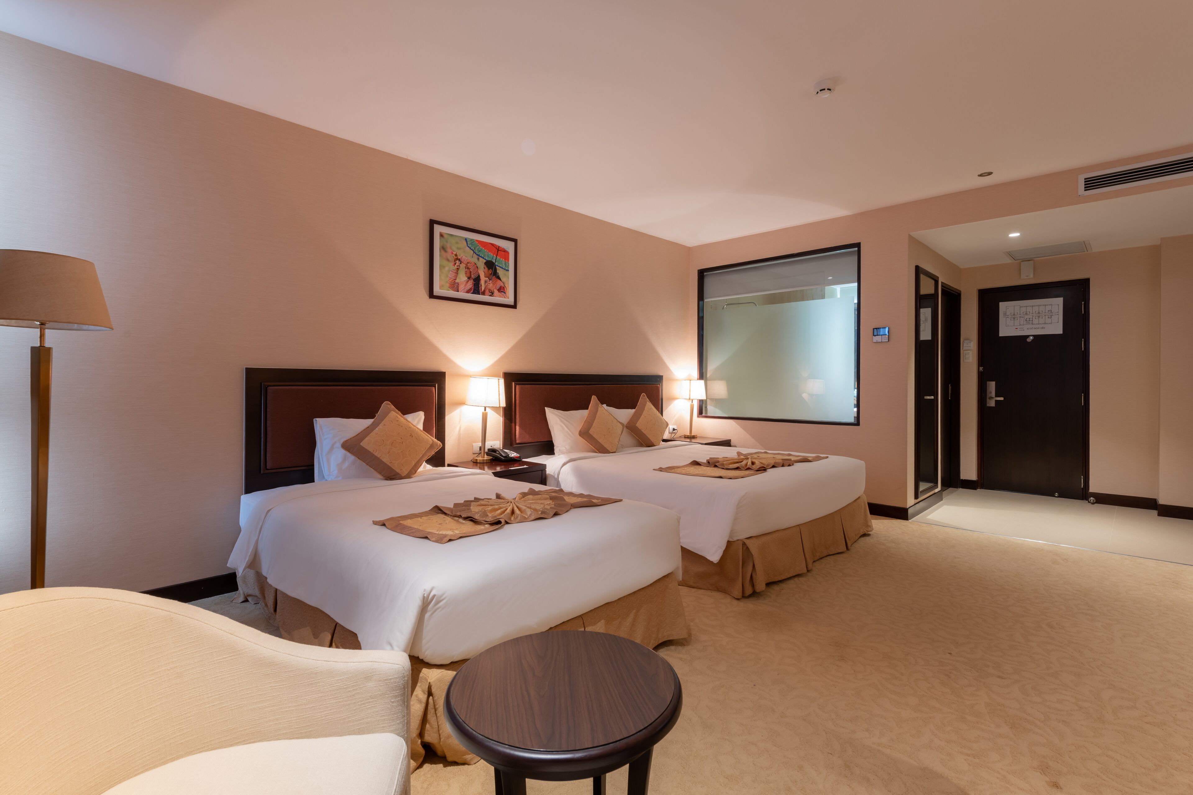 A hotel room with two beds, a small round table, and a lamp.
