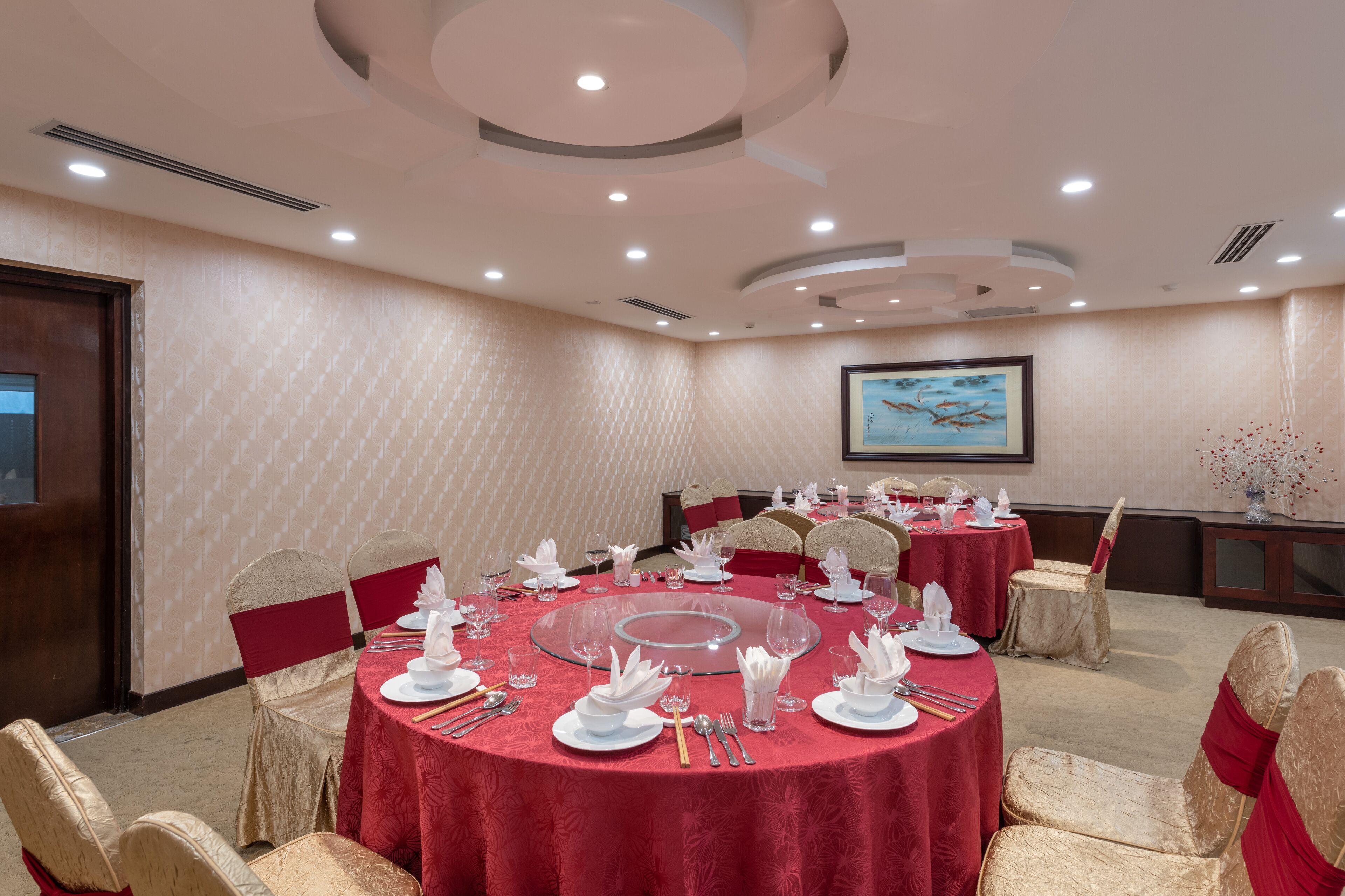 Uma sala de conferência com mesas redondas, toalhas vermelhas e cadeiras douradas.