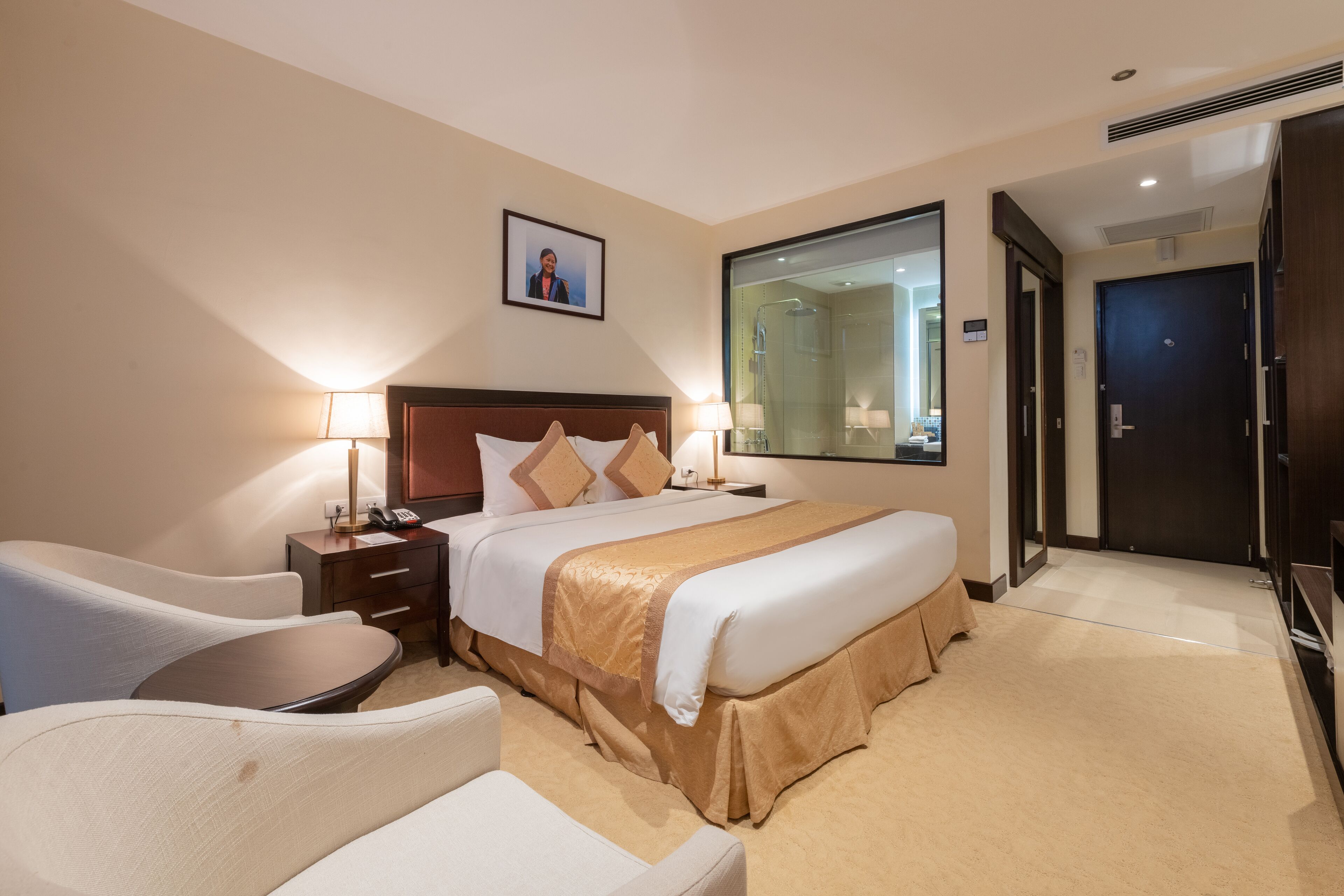 A hotel room with a bed, bedside tables, a desk, a chair, a large mirror, and a door.