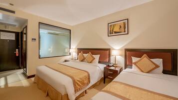 A hotel room with two beds, each with a wooden headboard, bedside tables with lamps, and a large window.
