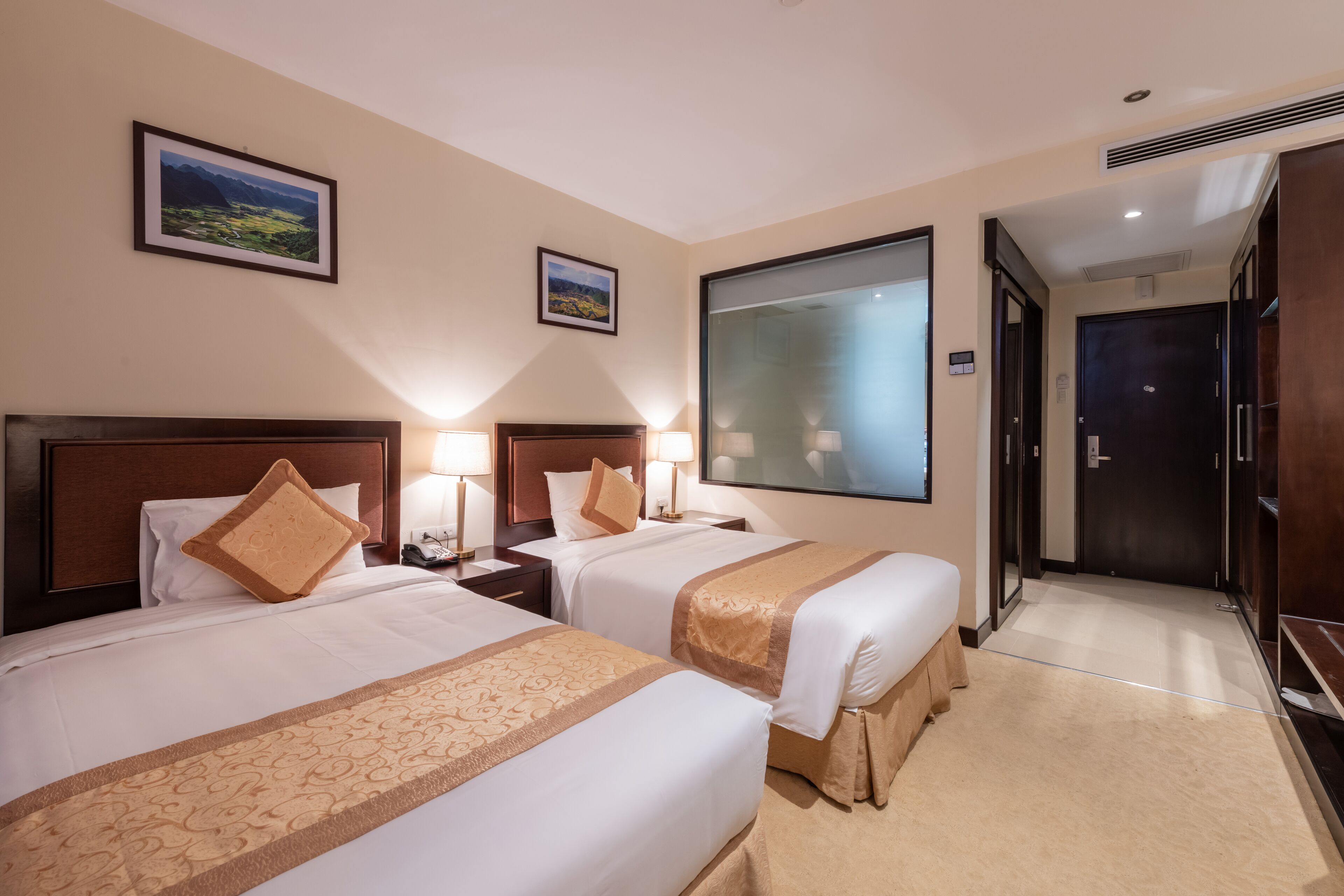 Une chambre d’hôtel avec deux lits, une grande fenêtre et une porte donnant sur un couloir.
