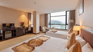 Habitación de hotel con dos camas, un escritorio, un televisor y un amplio ventanal con vistas.